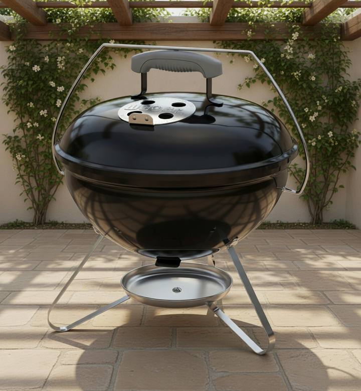 Black Weber Smokey Joe 14 kettle on a patio, lid on, chrome bail handle raised, silver ash catcher below the tripod legs