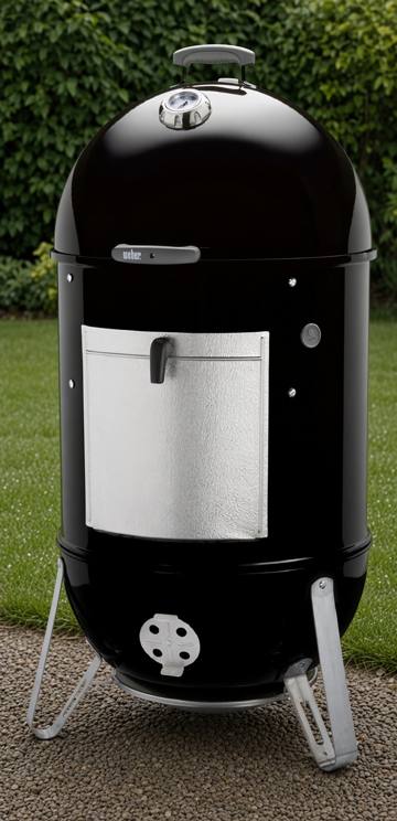 Weber Smokey Mountain Cooker Smoker 22 standing on gravel, black barrel, aluminum fuel door, lid thermometer