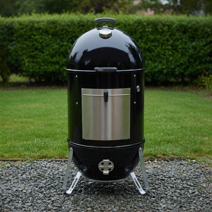 Weber Smokey Mountain Cooker Smoker 22 standing on gravel, black barrel, aluminum fuel door, lid thermometer