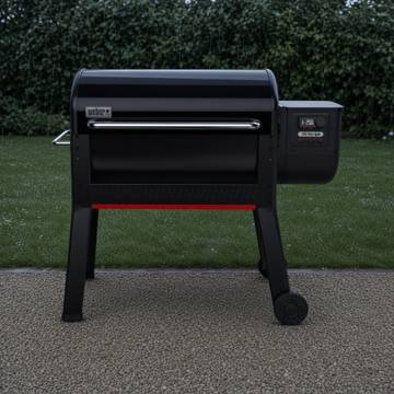 Black Weber Smoque XL pellet smoker on gravel beside a lawn, lid closed, lit controller on the right hopper, red stripe below