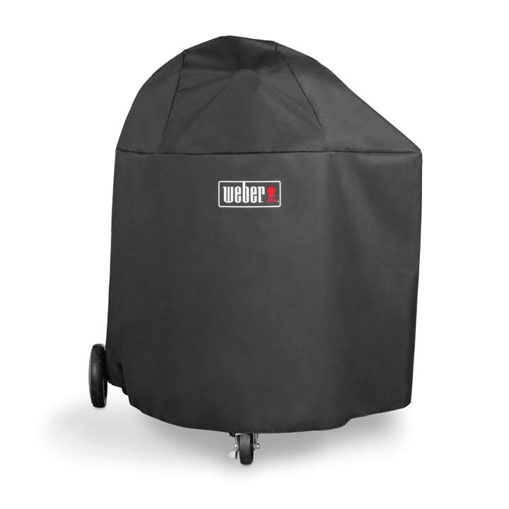 Black Weber cover with a logo patch pulled over a Summit kamado, two wheels and a front caster showing below the hem