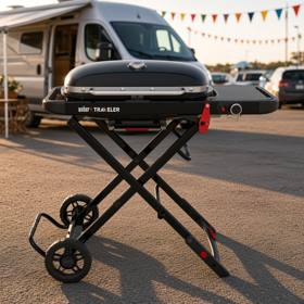 Weber Traveler portable gas grill standing on its folding frame behind a van, lid closed and side table out