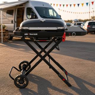 Weber Traveler portable gas grill standing on its folding frame behind a van, lid closed and side table out