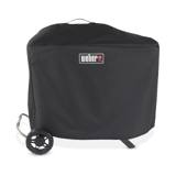 Black Weber Traveler Premium Grill Cover over a standing Traveler, top loop handle, one wheel and a leg showing below
